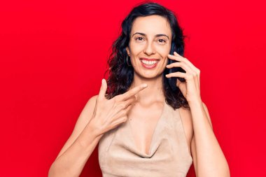 Genç, güzel, İspanyol bir kadın akıllı telefondan konuşuyor. Gülümsüyor, mutlu bir şekilde elini ve parmağını işaret ediyor. 
