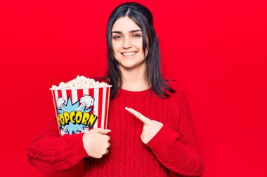 Patlamış mısır yiyen genç ve güzel bir kız mutlu mesut elini ve parmağını gösteriyor. 