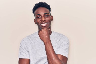 Gündelik giysiler giymiş genç Afro-Amerikan adam kameraya kendinden emin bakıyor kollarını kavuşturmuş ve çenesini kaldırmış bir şekilde gülümsüyor. Olumlu düşünmek. 