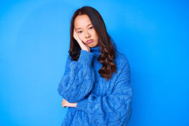 Genç, güzel Çinli bir kız, sıradan bir kazak giyip kollarını kavuşturarak depresyondan sıkılmış ve yorgun görünüyor.. 