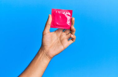 Genç İspanyol el, mavi arka planda kondom tutuyor..