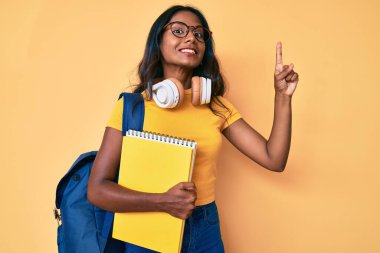 Sırt çantası ve kitaplarla gülümseyen Hintli genç bir kız. Mutlu yüzle işaret eden bir fikir ya da soru. 