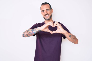 Dövmeli, sıradan kıyafetler giyen, aşık gülümseyen ve elleriyle kalp sembolü çizen genç yakışıklı bir adam. romantik kavram. 