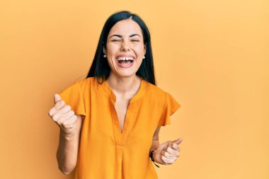 Güzel, genç bir kadın gündelik kıyafetler giyip çok mutlu ve heyecanlı bir şekilde kollarını kaldırıp, gülümseyerek ve başarı için çığlık atarak kazanan bir jest yapıyor. kutlama konsepti. 