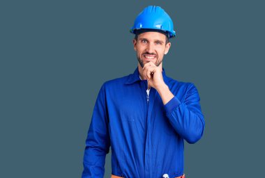 Genç, yakışıklı, işçi üniforması giyen, kasketli, kameraya kendinden emin, kollarını kavuşturmuş ve çenesini kaldırmış gülümseyen bir adam. Olumlu düşünmek. 