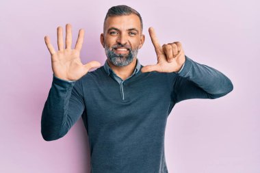 Orta yaşlı, sıradan kıyafetler giyen yakışıklı bir adam yedi numarayı gösterip işaret ederken kendinden emin ve mutlu bir şekilde gülümsüyor.. 