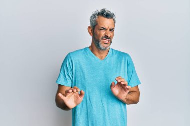 Orta yaşlı, gri saçlı, günlük kıyafetler giyen, tiksindirici, tiksindirici, tiksindirici bir yüz ifadesi takınan bir adam. Eller havada. 