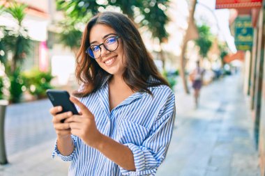 Genç İspanyol iş kadını şehirde akıllı telefon kullanarak mutlu gülümsüyor..