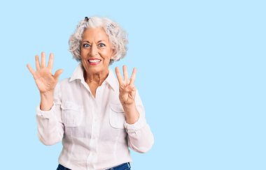 Yaşlı, gri saçlı, günlük kıyafetler giyen, 8 numaralı parmaklarıyla işaret eden, kendinden emin ve mutlu bir kadın.. 