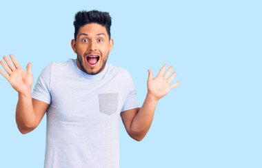 Yakışıklı Latin Amerikalı genç adam gündelik giysiler giyip çılgınlığı kutluyor ve başarı için hayrete düşüyor kolları açık ve gözleri açık heyecanla bağırıyor. Kazanan konsept 