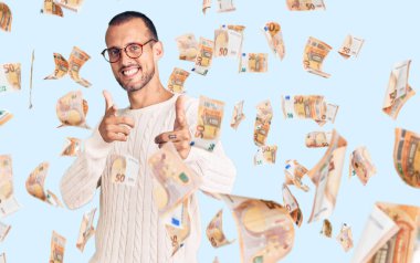 Sıradan kıyafetler giyen ve gözlüklü genç yakışıklı adam mutlu ve komik yüzüyle kamerayı işaret ediyor. iyi enerji ve titreşimler.