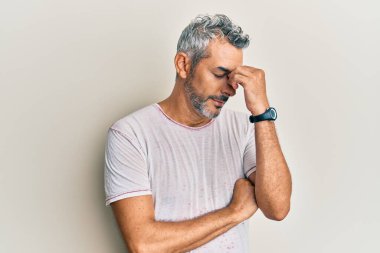 Orta yaşlı, gri saçlı, günlük kıyafetler giyen, burnu ve gözleri ovuşturan, yorgunluk ve baş ağrısı çeken bir adam. Stres ve hüsran kavramı. 