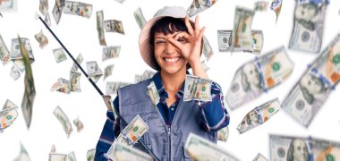 Kısa saçlı, balıkçı teçhizatı takan genç esmer kadın gülümsüyor.