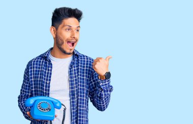 Yakışıklı Latin Amerikalı genç adam, elinde antika bir telefonla baş parmağını kaldırıyor ve ağzı açık gülümsüyor. 