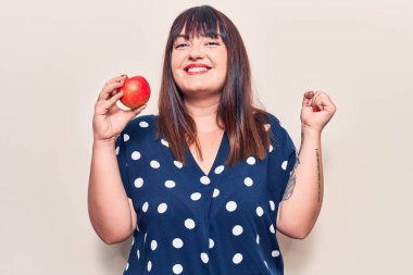 Genç ve cüsseli bir kadın kırmızı elma tutuyor gururla bağırıyor, zaferi kutluyor ve başarıyı kollarını kaldırarak kutluyor. 