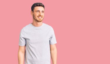 Yüzünde gülümseme, doğal bir ifade olan, sıradan tişörtler giyen yakışıklı genç bir adam. Kendinden emin gülen. 