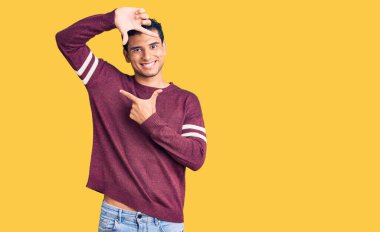 Gündelik kıyafetler giyen İspanyol yakışıklı genç adam gülümseyerek elleri ve parmakları gülen yüzle çerçeve yapıyor. yaratıcılık ve fotoğrafçılık kavramı. 