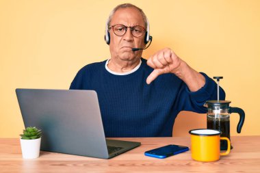 Ofiste çalışan gri saçlı yaşlı yakışıklı bir adam. Operatör kulaklığı takıyor. Kızgın bir yüzü var. 