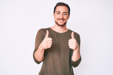 Gündelik kıyafet giyen yakışıklı bir adam. Başarı işareti yapıyor. Elleriyle olumlu jest yapıyor. Neşeli ifade ve kazanan jest. 