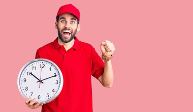 Sakallı yakışıklı adam büyük bir saat tutuyor gururla bağırıyor zaferi kutluyor ve başarıyı kollarını kaldırarak kutluyor. 