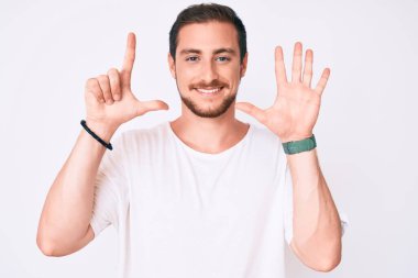 Gündelik beyaz tişört giyen genç yakışıklı adam yedi numarayı gösterip işaret ederken kendinden emin ve mutlu bir şekilde gülümsüyor.. 