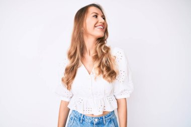 Sarı saçlı, sıradan yaz kıyafetleri giyen, yüzünde gülümsemeyle yan yana bakan beyaz bir kadın. Kendinden emin gülen. 