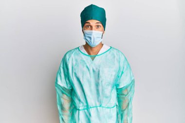 Cerrah üniforması ve tıbbi maske takan genç yakışıklı adam şaşkınlık ifadesi, korku ve heyecanlı yüz ifadesiyle korkmuş ve şok olmuştu.. 