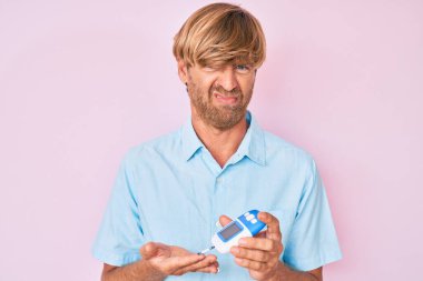 Genç sarışın adam glikoz ölçer kullanıyor şüpheci ve gergin, sorun yüzünden surat asıyor. negatif kişi. 