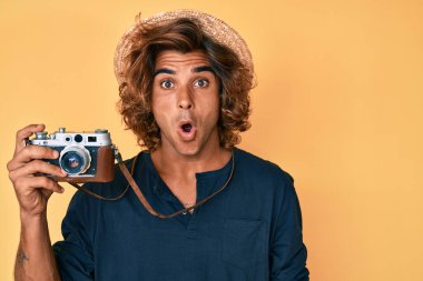 Şapkalı genç İspanyol adam elinde eski bir kamera tutuyor. Korkmuş ve şaşırmış bir şekilde ağzı açık, inançsız bir yüz. 