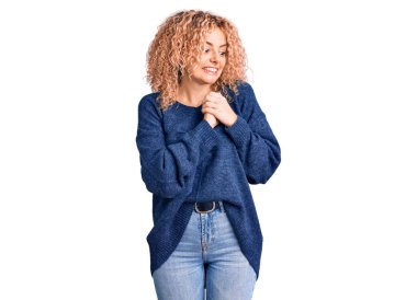 Kıvırcık saçlı, sıradan bir kazak giyen, elleri çenesinde gergin ve heyecanlı bir şekilde yan tarafa bakan genç sarışın kadın. 