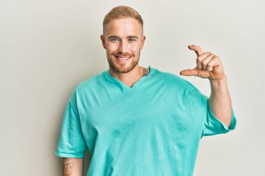 Gündelik kıyafetler giyen, gülümseyen, kendine güvenen, el hareketi yapan, parmaklarıyla işaret yapan ve kameraya bakan genç beyaz bir adam. ölçüm kavramı. 