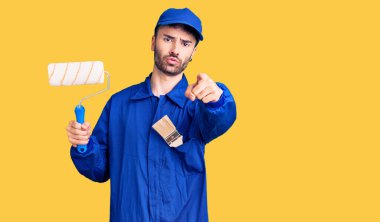 Ressam üniforması giyen genç İspanyol adam kamerayı işaret eden bir silindir tutuyor ve sen kendine güvenen ciddi bir hareket yapıyorsun. 