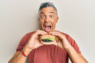 Yakışıklı, orta yaşlı, olgun bir adam lezzetli klasik bir burger yiyor. Çılgınlığı kutluyor ve başarıya hayret ediyor. Gözleri açık, heyecanlı bir şekilde bağırıyor.. 