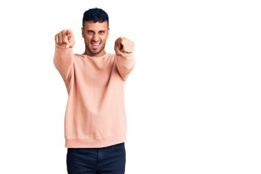 Gündelik kıyafetler giyen genç İspanyol adam seni ve kamerayı parmaklarıyla göstererek mutlu ve mutlu gülümsüyor. 