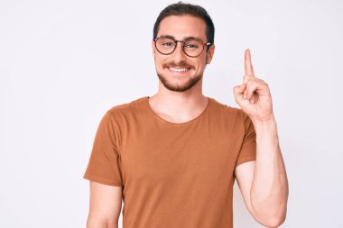 Gündelik kıyafetler giyen ve gözlüklü genç yakışıklı adam başarılı bir fikirle işaret ediyor. Heyecanlı ve mutlu. Bir numara.. 