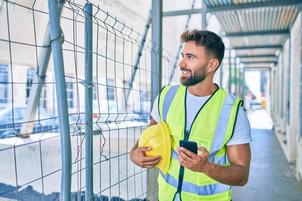 Young hispanic architect man holding blueprint using smartphone at street of city