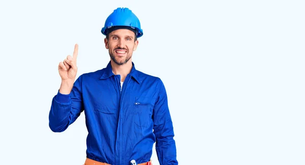労働者の制服を着た若いハンサムな男と堅い帽子は成功した考えと指を指している 興奮して幸せよ 第1位 — ストック写真