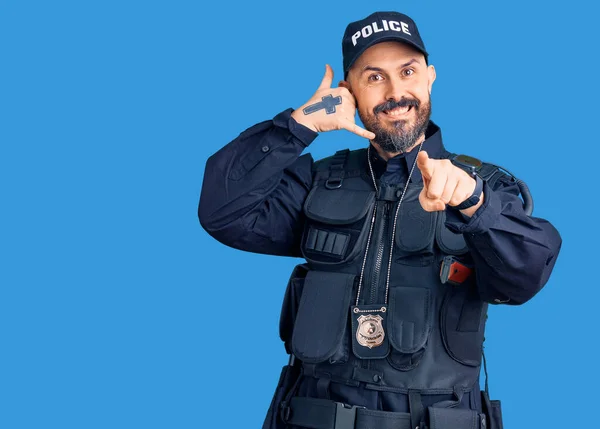 Young handsome man wearing police uniform smiling doing talking on the telephone gesture and pointing to you. call me.