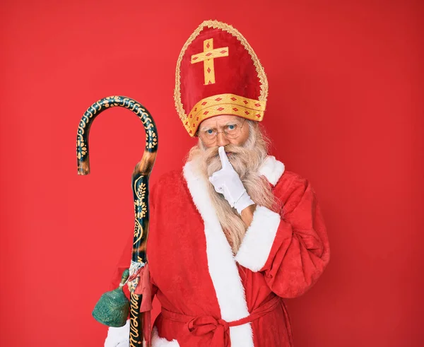 白髪で長い髭を生やした年配の男性は 唇に指で静かにするように頼む伝統的な聖人ニコラスの衣装を着ていました 沈黙と秘密の概念 — ストック写真