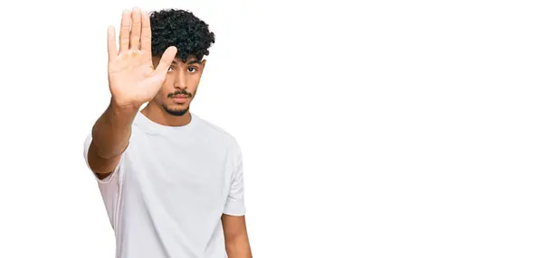 年轻的阿拉伯男子穿着随意的白色T恤衫 用手的手掌停止歌唱 用消极而严肃的手势警告人 — 图库照片