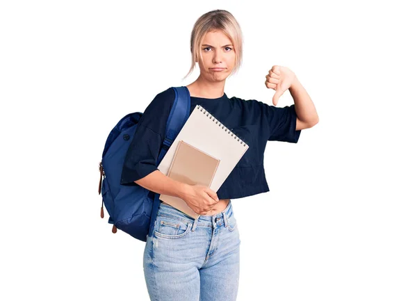 若い美しいブロンドの女性を身に着けている学生のバックパックを保持ノートブックで怒っている顔 否定的な兆候を示す嫌いで親指ダウン 拒絶概念 — ストック写真