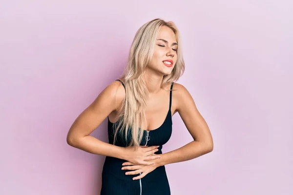 Beautiful caucasian blonde girl wearing sexy party dress with hand on stomach because nausea, painful disease feeling unwell. ache concept.