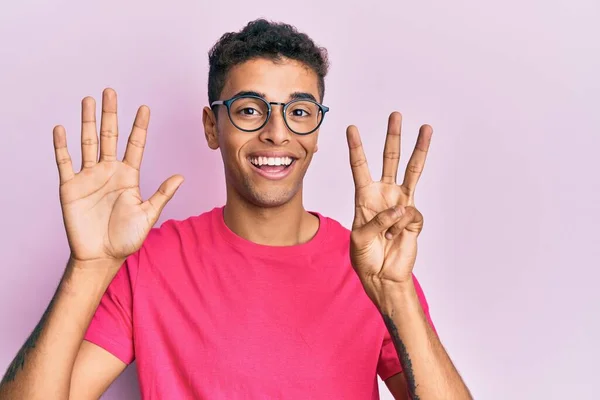 若いですハンサムなアフリカ系アメリカ人男性身に着けています眼鏡上のピンクの背景表示と指差す指数8ながら笑顔自信と幸せ — ストック写真