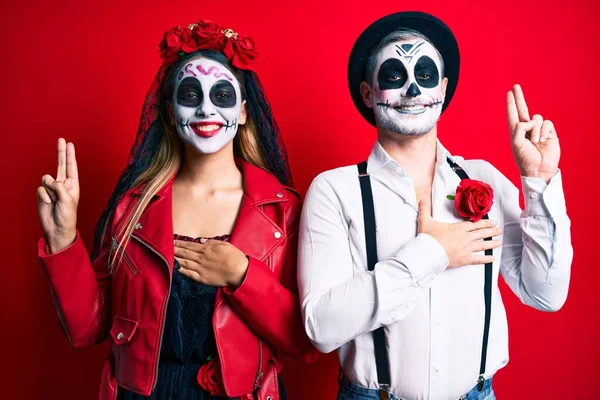 Casal vestindo fantasia de dia dos mortos sobre vermelho sorrindo fazendo  moldura com mãos e dedos com cara de feliz. conceito de criatividade e  fotografia.