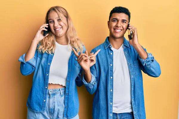 Genç, ırklar arası bir çift akıllı telefondan konuşuyor. Gülümsüyor, mutlu bir şekilde işaret ediyor. 