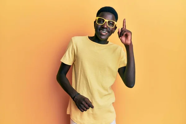 若いアフリカ系アメリカ人の男性は カジュアルな服と眼鏡をかけて成功したアイデアで指を指しています 興奮して幸せよ 第1位 — ストック写真