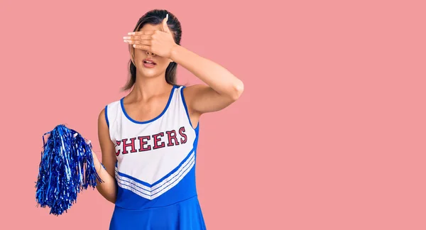 Young beautiful woman wearing cheerleader uniform covering eyes with hand, looking serious and sad. sightless, hiding and rejection concept