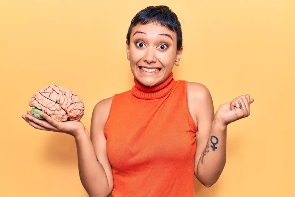 Young woman holding brain screaming proud, celebrating victory and success very excited with raised arm