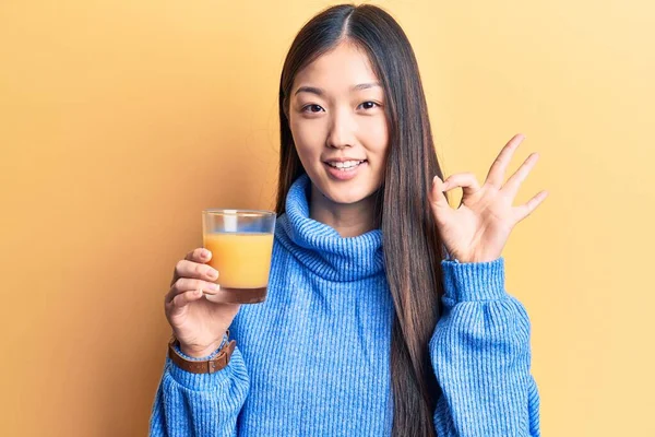 年轻美丽的中国女人喝着一杯橙汁 手拿着手签 微笑着表示友好的姿态 是极好的象征 — 图库照片