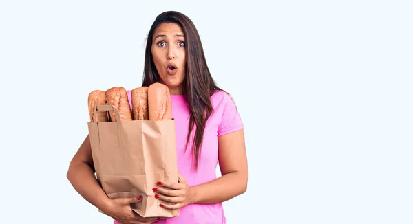 Young Beautiful Brunette Woman Holding Delivery Bag Bread Scared Amazed — Stock Photo, Image